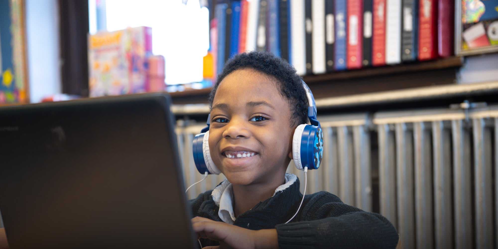 Smiling student wearing headphones while working on a laptop.