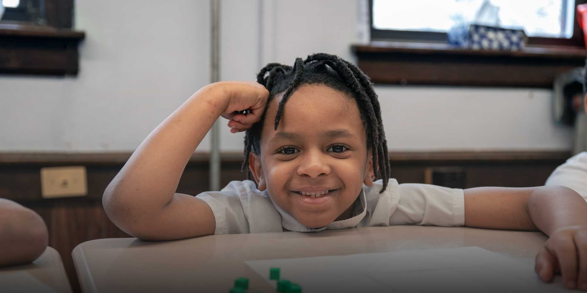 Smiling Lake Erie Prep student resting an arm on a classroom desk.